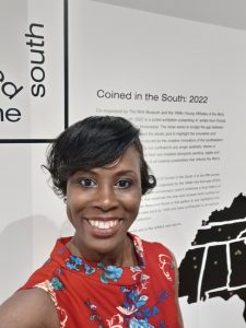 Sukenya Best smiling for photo in front of text reading "Coined in the South 2022"