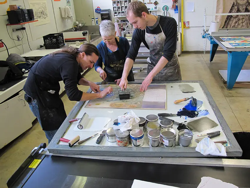 Karen Kunc works with Clifton Riley (MFA ‘13) and Daniel Ogletree (MFA ‘14) to ink Kunc’s woodcut from 2012.