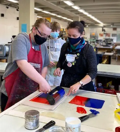 Two people masked working at a printmaking table