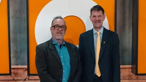 Two men posing for a photo at an event in front of orange decorative lettering