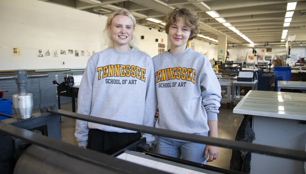 Two female students in an art studio space wearing gray sweatshirts that say Tennessee School of Art