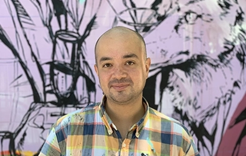 Headshot photo of a man with a painting behind him