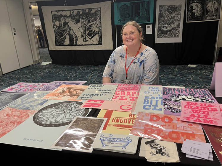 A woman sitting behind a table with artwork spread out on the table