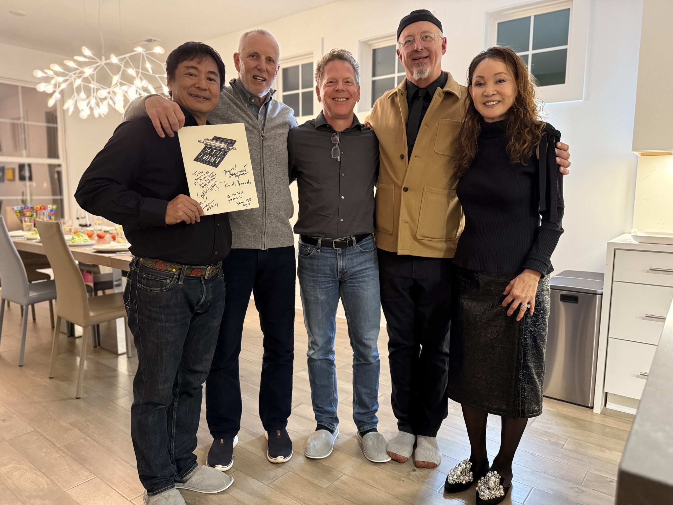 Five people stand in a kitchen with a signed print.