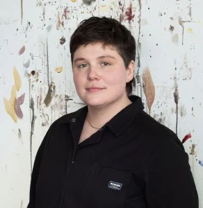A headshot of a person standing against a painted background