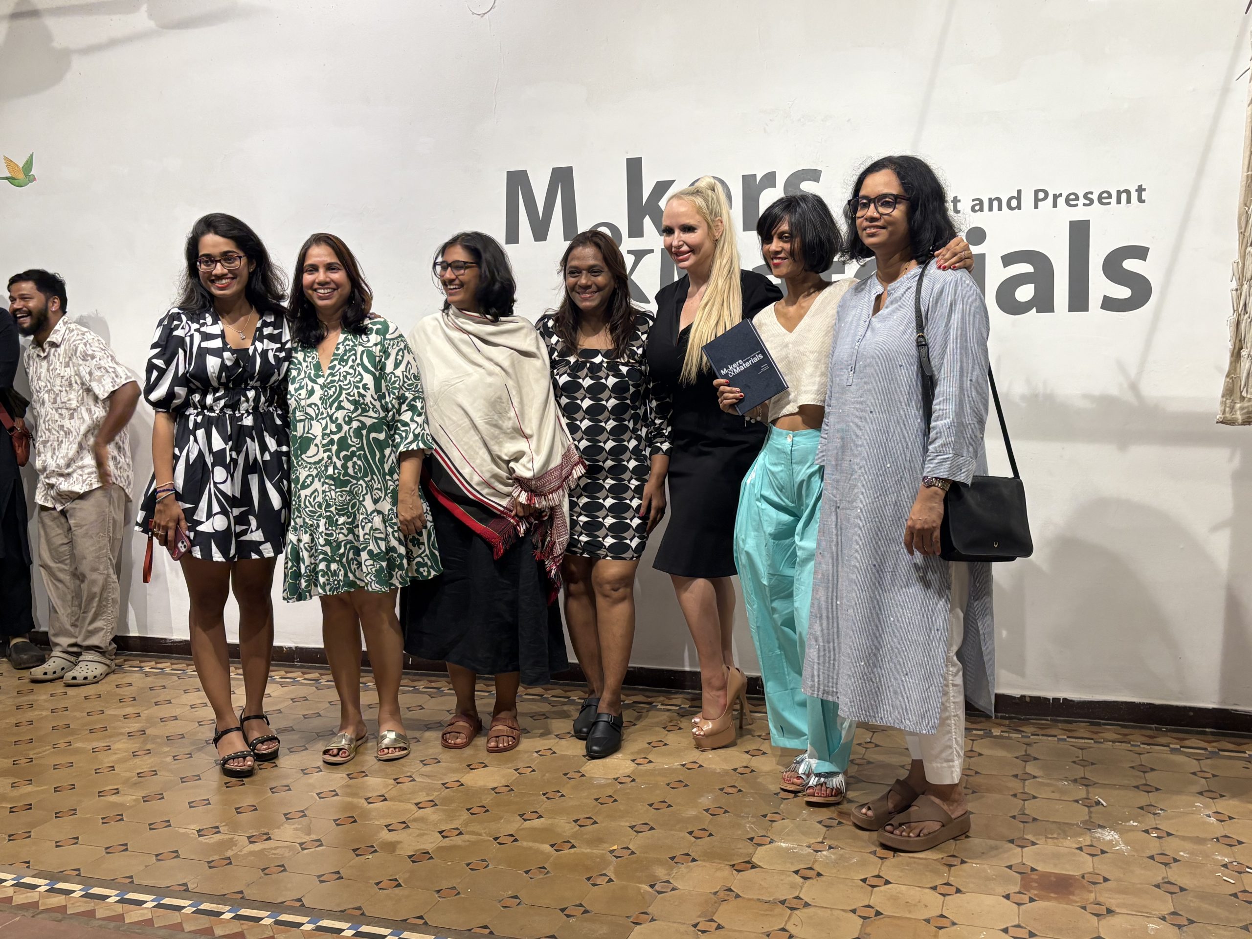 A group of women stand infront of an exhibition sign reading Makers and Materials: Goa Past and Present.
