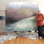 A woman stands in front of large landscape painting