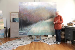 A woman stands in front of large landscape painting