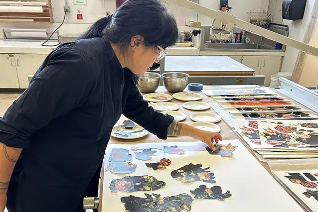 Collet Fu surrounds herself with print materials on a table as she works on making a book. 