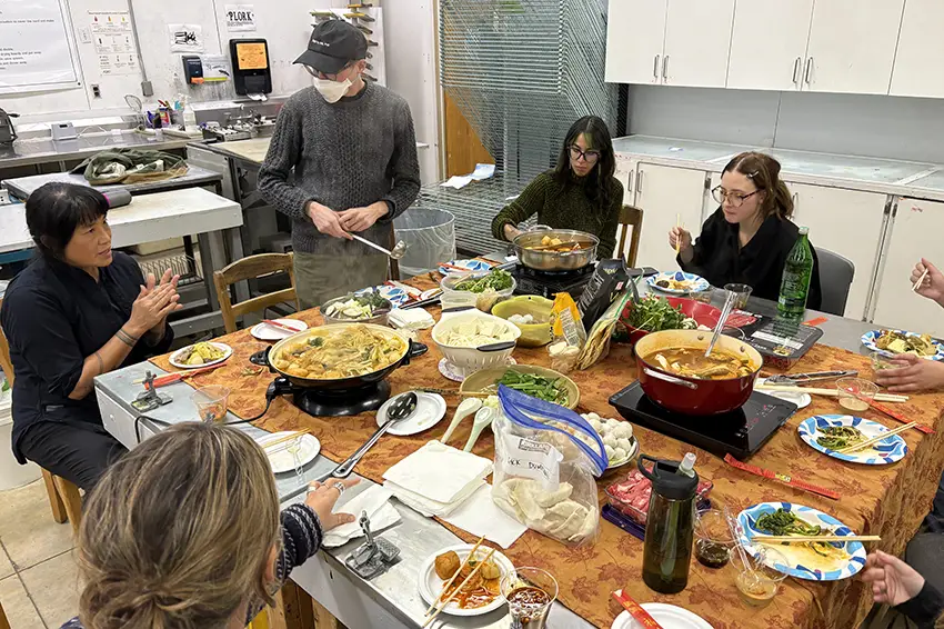Graduate students sit around a square table  while eating a potluck together. 