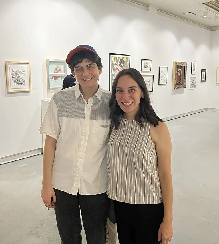 J Leigh Garcia and a UT alumni take a photo together inside an art gallery with various pieces lining the wall behind them. 