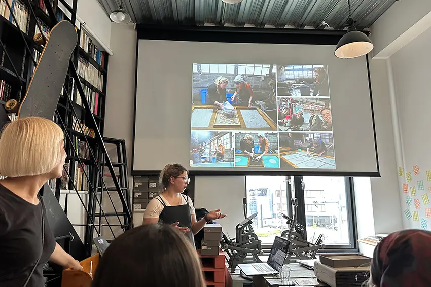 Raluca Iancu engages in an artist talk, speaking with a project of photos and surrounded by people. 
