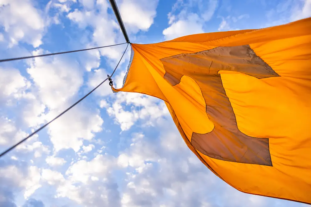 The Power T, orange flag, flies against a blue, cloudy sky. 