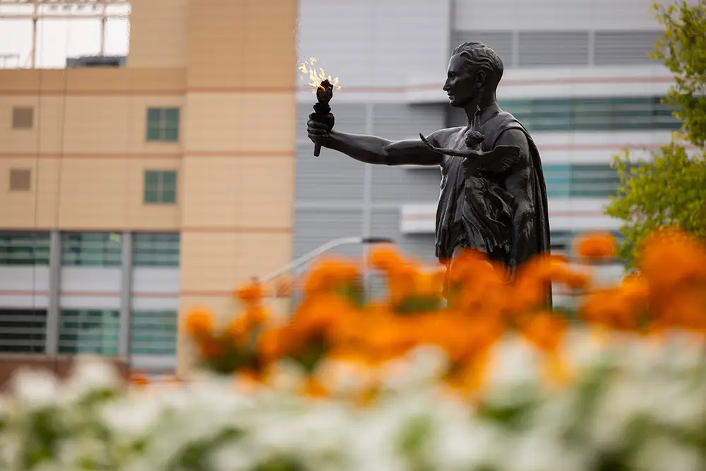 The Torchbearer statue holds a flame in front of orange flowers. 
