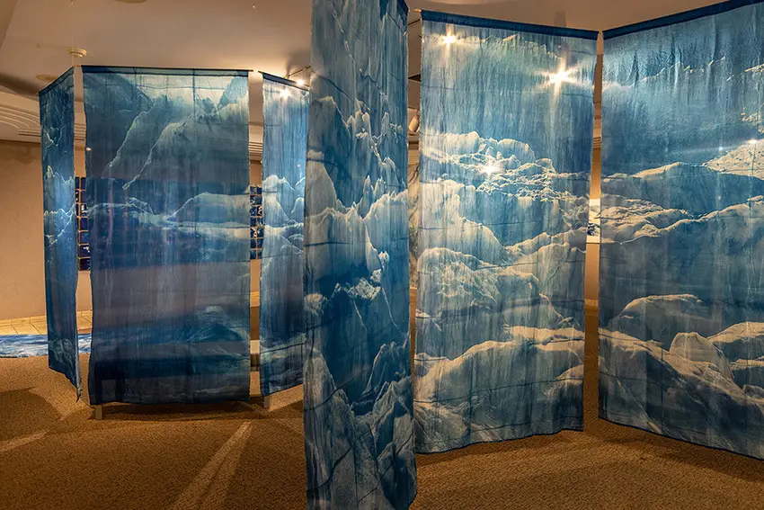 Artistic images of glaciers hang from cyanotype in an art gallery. 